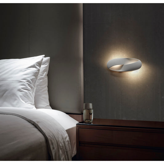 Applique murale LED blanche au design moderne et enveloppant, installée à côté d’un lit dans une chambre élégante. Éclairage doux et diffus créant une atmosphère apaisante.