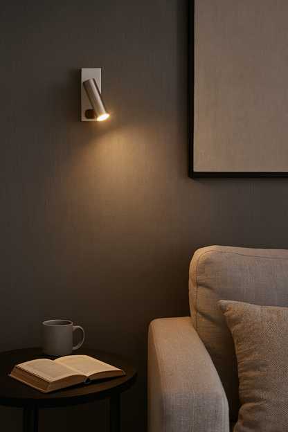 Applique murale LED en acier brossé installée dans un coin lecture cosy. Éclairage directionnel chaud de 3000K, avec interrupteur intégré, idéale comme lampe de chevet.