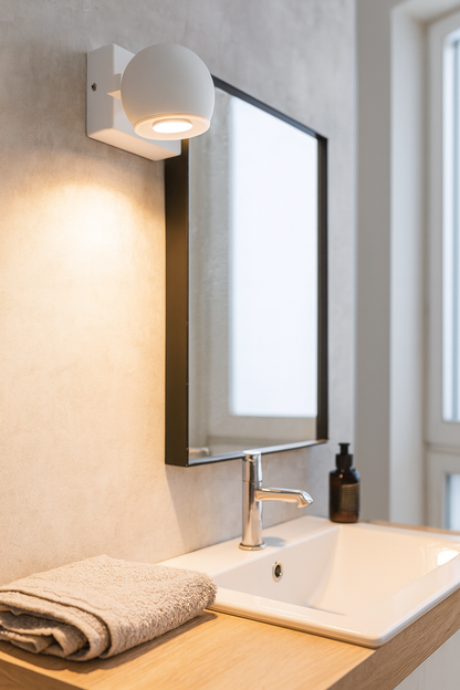 Applique murale blanche au design arrondi installée dans une salle de bain moderne, diffusant une lumière douce et élégante au-dessus d’un miroir.