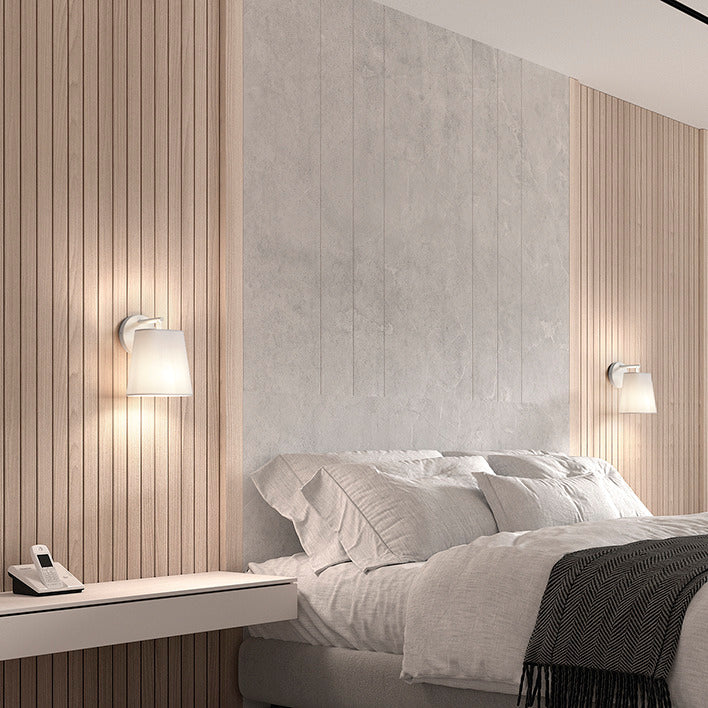 Applique murale NEMO blanche avec abat-jour en verre, installée en tête de lit dans une chambre moderne et élégante.