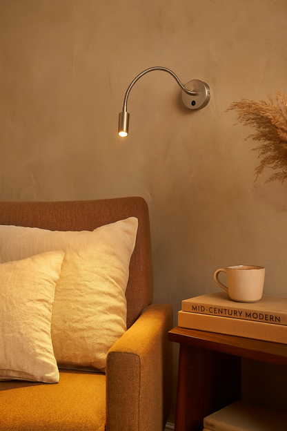 Applique murale à bras flexible en nickel satiné, éclairage chaud dirigé, mise en scène dans un coin lecture cosy avec fauteuil et livres.