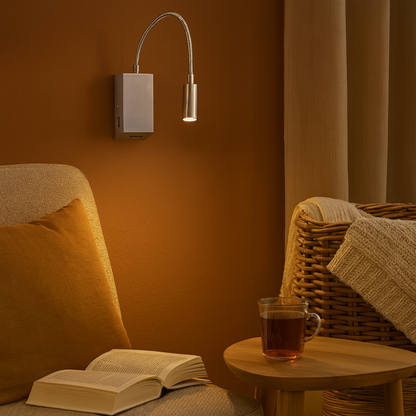 Applique murale en nickel satiné fixée au mur d’une chambre cosy, diffusant une lumière chaude sur un livre ouvert. L’ambiance est douce et apaisante, idéale pour un coin lecture élégant.