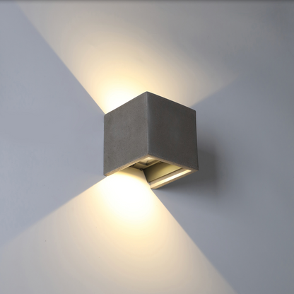 Applique murale extérieure Perseo en finition gris ciment, design minimaliste et élégant, diffusant une lumière douce et chaleureuse résistante aux intempéries.