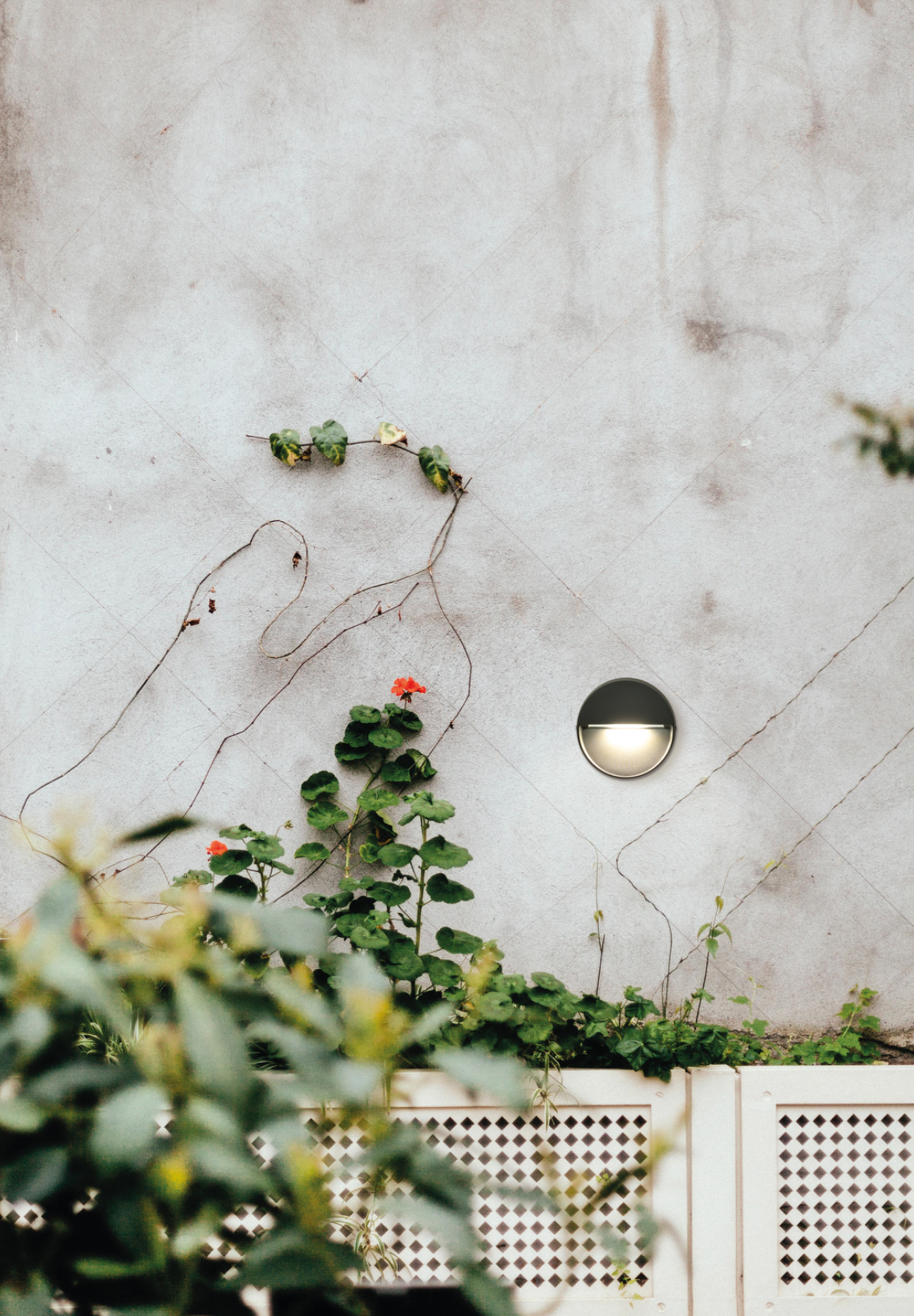 Balise murale extérieure Spica ronde et discrète, diffusant une lumière douce et ciblée idéale pour baliser les zones de passage et structurer les extérieurs avec élégance.