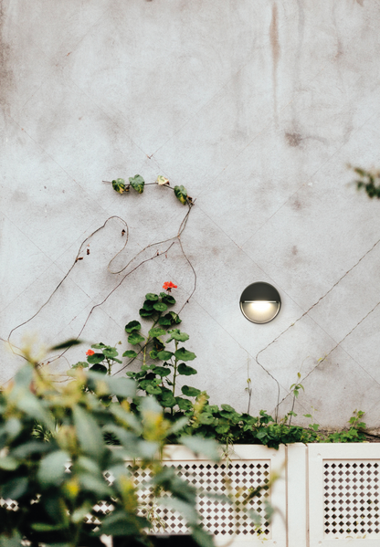 Balise murale extérieure Spica ronde et discrète, diffusant une lumière douce et ciblée idéale pour baliser les zones de passage et structurer les extérieurs avec élégance.