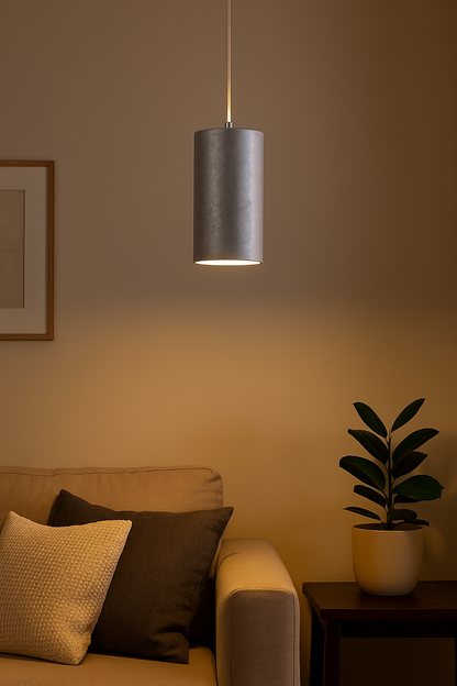 Suspension cylindrique argentée Selma diffusant une lumière chaude dans un salon moderne aux tons gris et bois clair, pièce maîtresse de la décoration intérieure contemporaine.